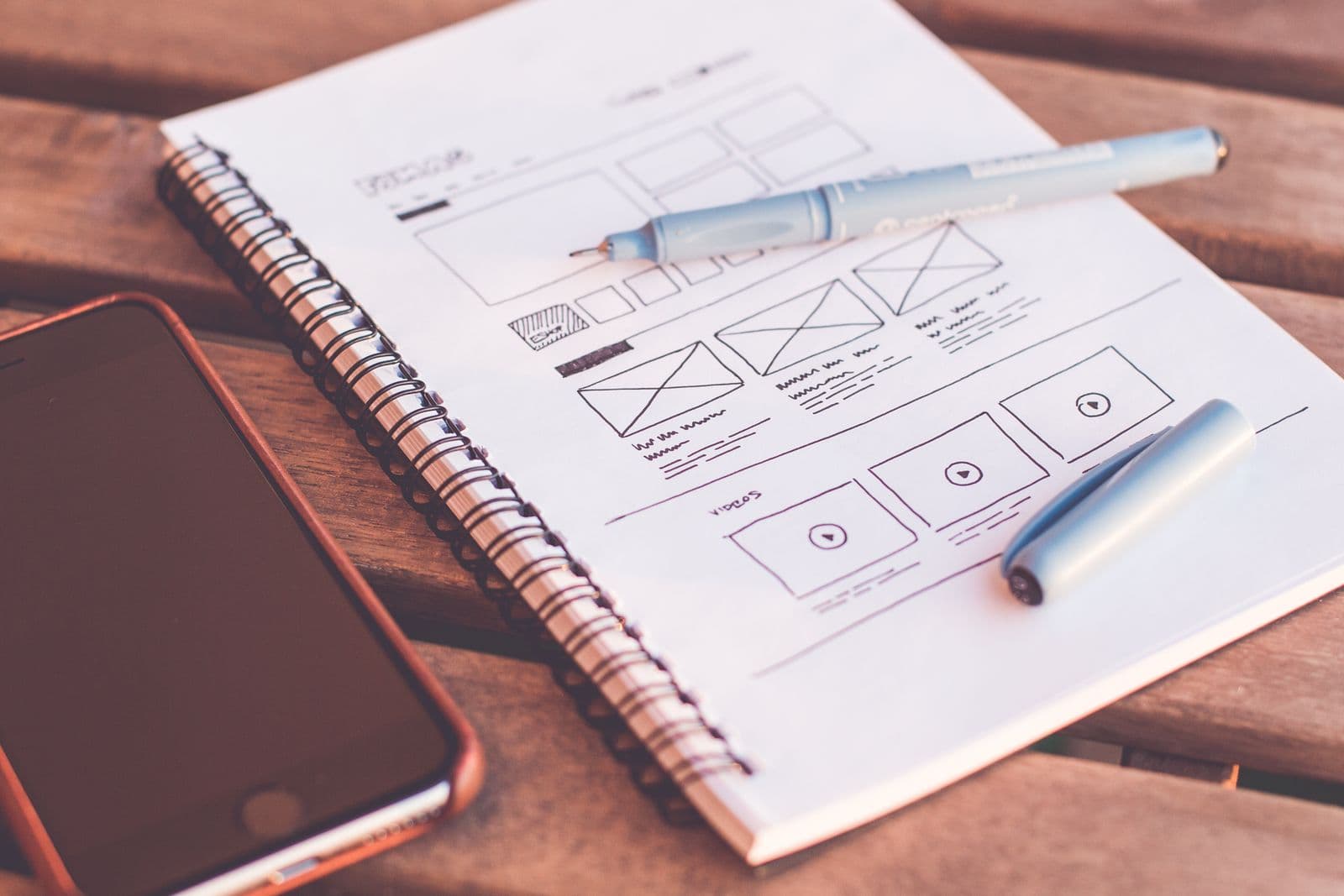 A designer's desk with a wireframe sketch, notebook and phone — the studio's working setup